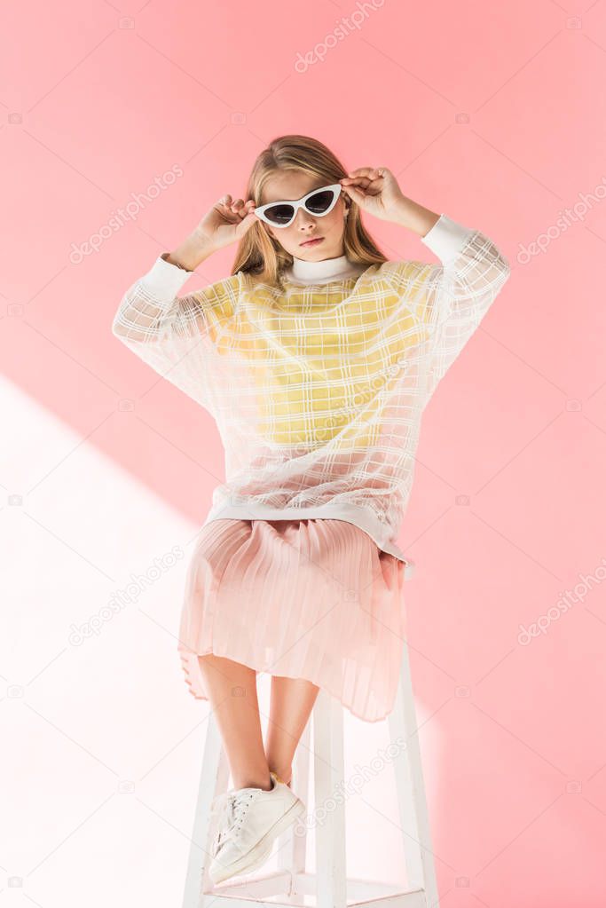 adorable fashionable child posing in sunglasses on stool on pink 