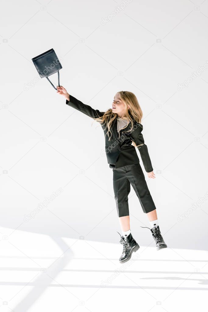 fashionable child in black suit flying with bag on grey