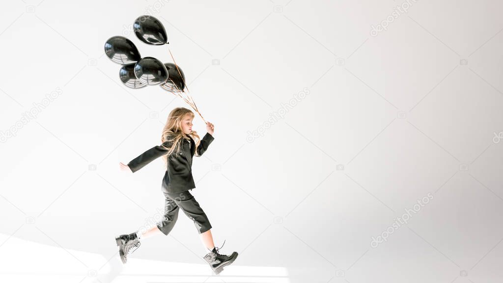 fashionable kid running with black balloons on grey