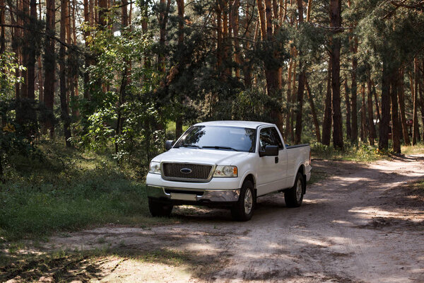 белый автомобиль на тропе в осеннем лесу с соснами
