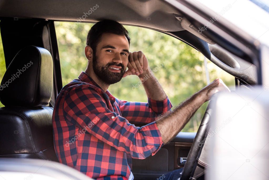 smiling bearded man driving pickup truck in forest