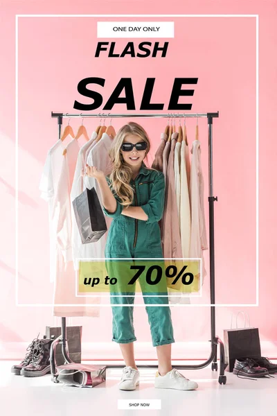 stylish child in overalls and sunglasses standing with shopping bag near clothes and footwear in boutique, flash sale banner concept