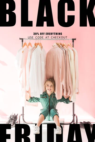 Cheerful Charming Kid Trendy Overalls Sitting Clothes Hangers Black Friday — Stock Photo, Image