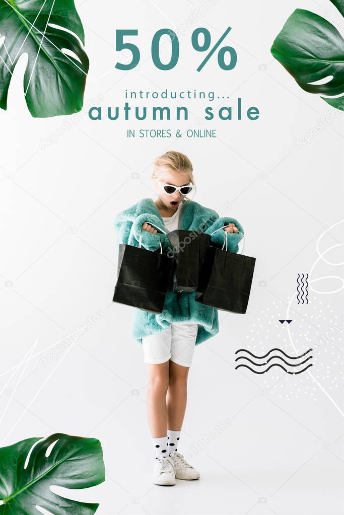 shocked kid in stylish fur coat looking into black shopping bags isolated on white, autumn sale banner concept