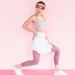 Attraktiva eleganta idrottskvinna i visiret hatt gör övning på pink