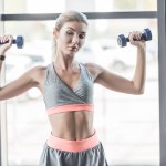 Pretty young woman exercising with dumbbells at gym