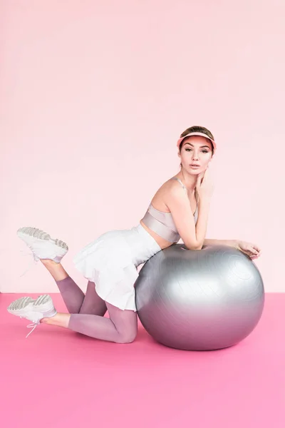 Hübsche Athletin Mit Schirmmütze Posiert Neben Grauem Fitnessball Auf Rosa lizenzfreie Stockbilder