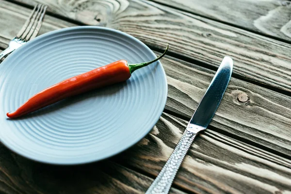 Красный перец чили на тарелке с ножом и вилкой на деревянном столе — стоковое фото
