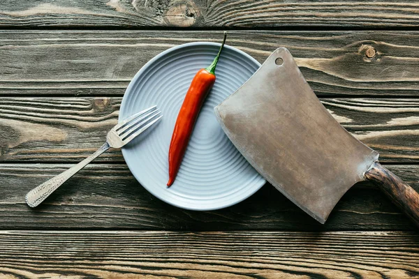 Red hot pepper served on plate with cleaver and fork on wooden table — Stock Photo