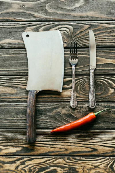 Silverware and cleaver with red chili pepper on wooden table — Stock Photo
