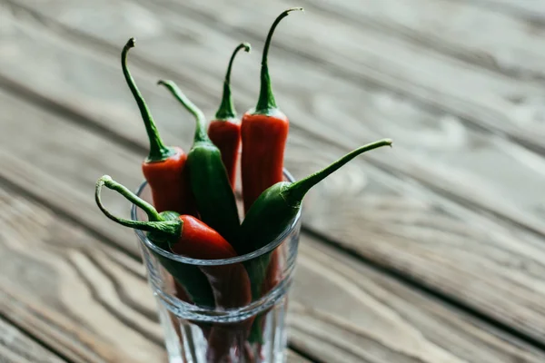 Bunch of peppers in glass on wooden table — Stock Photo