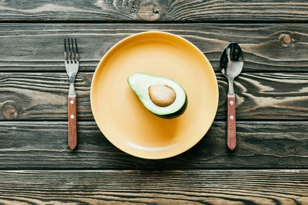 Avocado served on plate with spoon and fork on wooden table — Stock Photo