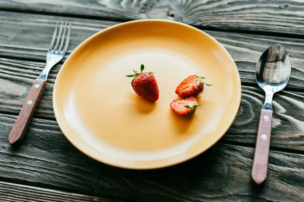 Rote Erdbeeren auf Teller mit Löffel und Gabel auf Holztisch serviert — Stockfoto