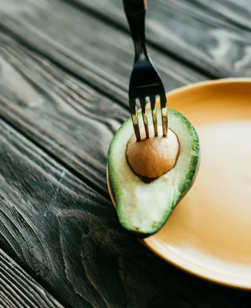 Fork in avocado on plate on wooden table — Stock Photo