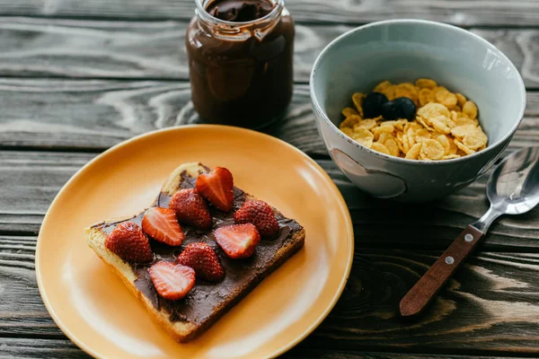 Flocos de milho e torradas com morangos e manteiga de chocolate na mesa de madeira — Fotografia de Stock