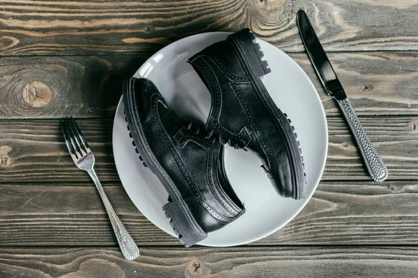 Chaussures couchées sur assiette avec couverts sur table en bois — Photo de stock