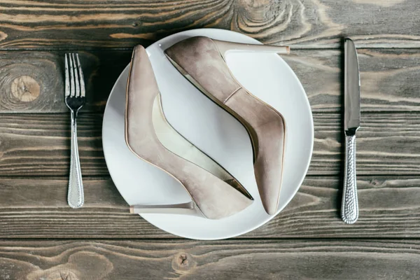 Damenabsatzschuhe auf Teller mit Besteck auf Holztisch — Stockfoto