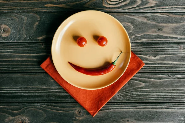 Placa con sonrisa hecha de pimienta y tomates en servilleta naranja - foto de stock