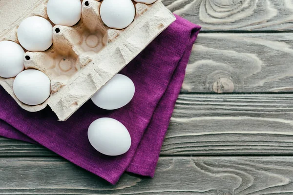 Carton box with white eggs on purple napkin — Stock Photo