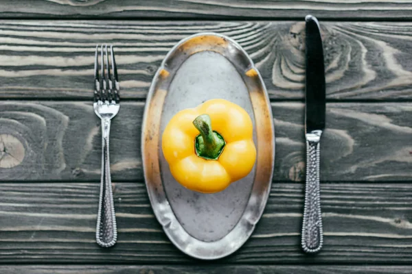 Pimiento amarillo servido en plato con cuchillo y tenedor sobre mesa de madera - foto de stock