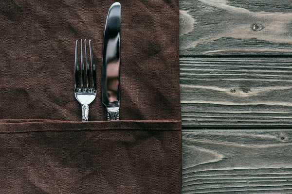 Набор столовых приборов с коричневой салфеткой на деревянном столе — стоковое фото