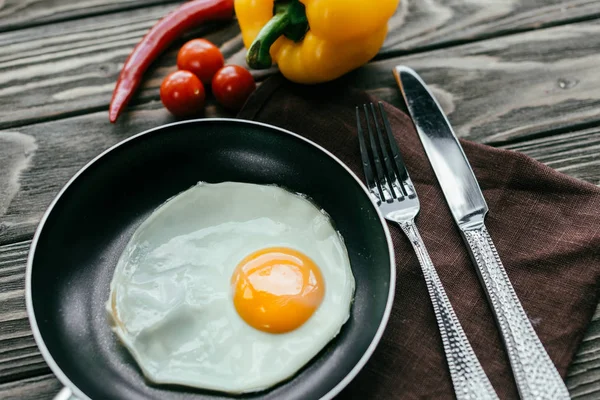 Panela com ovo frito em guardanapo têxtil com talheres e legumes — Fotografia de Stock