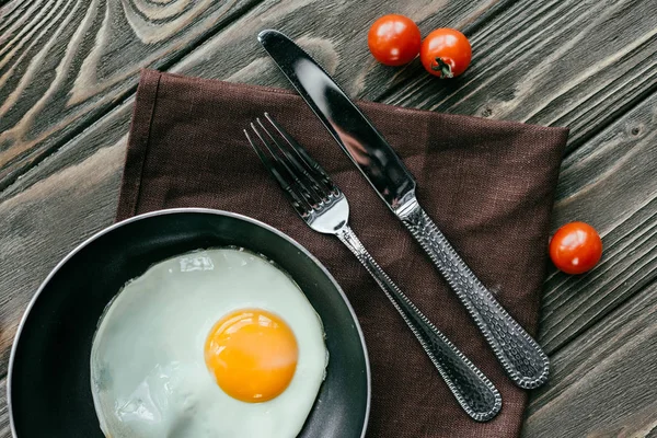 Sartén con huevo y cubiertos sobre mesa de madera con tomates - foto de stock