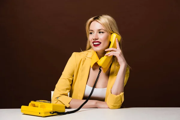 Schönes lächelndes blondes Mädchen, das am alten Telefon spricht und wegsieht auf braun — Stockfoto