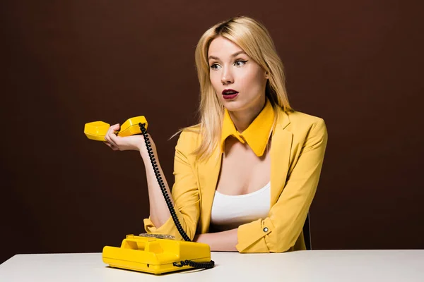 Überrascht blondes Mädchen hält gelben Hörer und schaut weg auf braun — Stockfoto