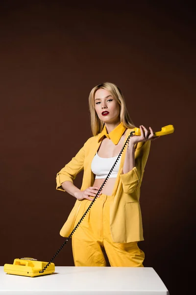 Schöne stilvolle blonde Frau mit gelben Hörer und Blick auf die Kamera auf braun — Stockfoto