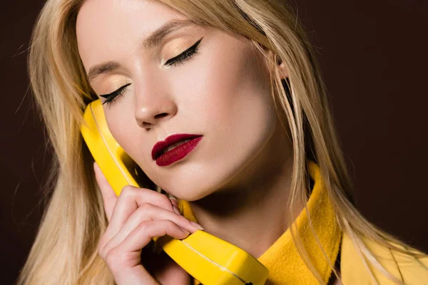 Close-up view of beautiful stylish blonde woman with closed eyes holding handset on brown — Stock Photo