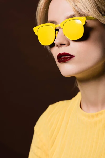 Retrato de bela menina loira vestindo óculos escuros amarelos isolados em marrom — Fotografia de Stock