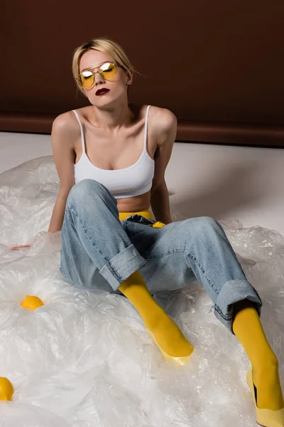 Belle jeune femme blonde élégante en lunettes de soleil jaunes posant en studio — Photo de stock