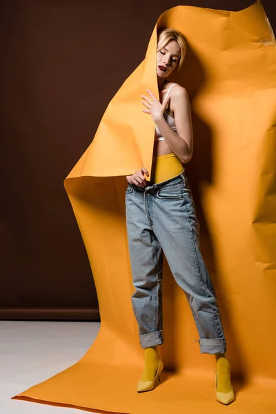 Sensual young blonde woman with closed eyes posing with orange paper on brown — Stock Photo