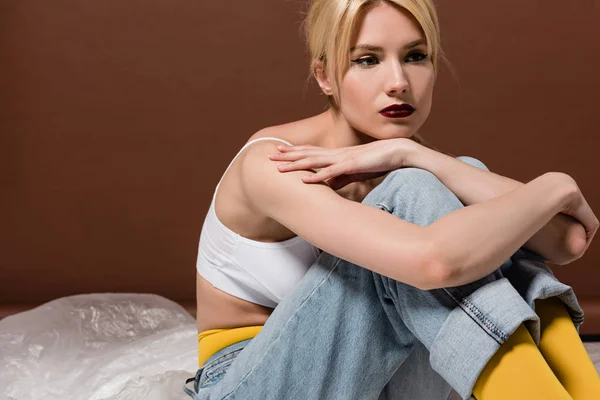 Pensive young blonde woman sitting and looking away on brown — Stock Photo