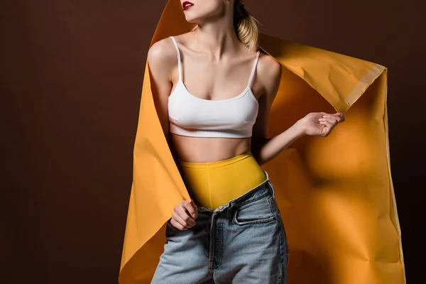 Cropped shot of seductive stylish girl posing with orange paper isolated on brown — Stock Photo