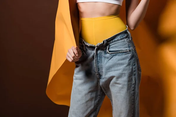 Ritagliato colpo di elegante giovane donna in posa con carta arancione isolato su marrone — Foto stock