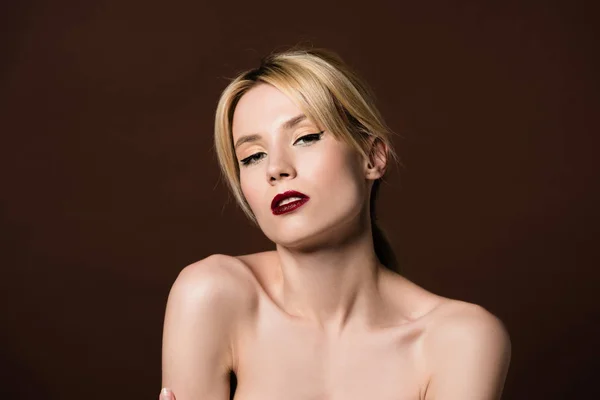 Портрет красивой голой молодой блондинки, смотрящей в камеру, изолированную от коричневого — стоковое фото