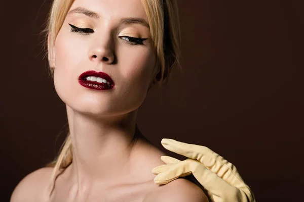 Рука в жовтій рукавичці торкається чуттєвої гола блондинка ізольована на коричневому — стокове фото