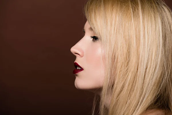 Side view of beautiful young blonde woman looking away isolated on brown — Stock Photo