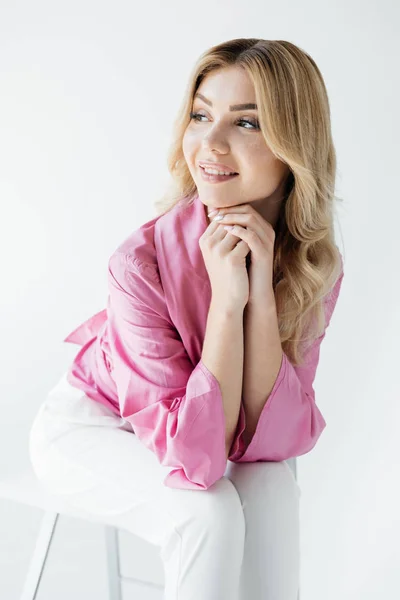 Beautiful young pensive woman in stylish clothing sitting on white chair on white backdrop — Stock Photo