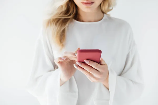 Tiro recortado de la mujer en ropa blanca con el teléfono inteligente en el fondo gris - foto de stock