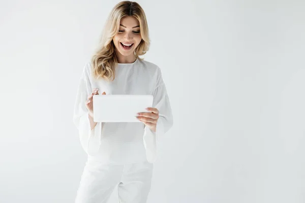 Приваблива весела жінка в білому одязі за допомогою планшета ізольована на сірому — стокове фото