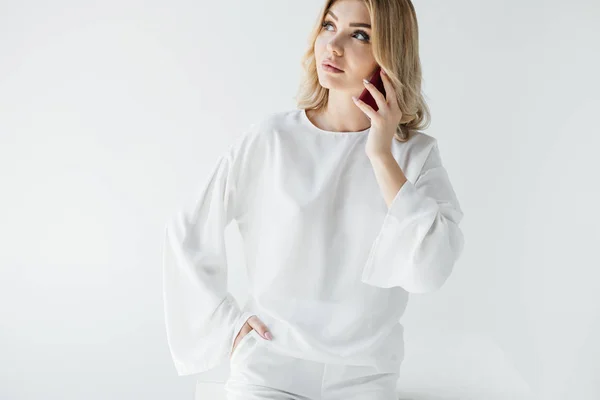 Portrait of blond woman in white clothing talking on smartphone isolated on grey — Stock Photo