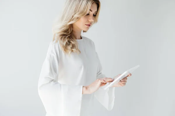 Молода приваблива жінка в білому одязі, використовуючи планшет на сірому фоні — стокове фото