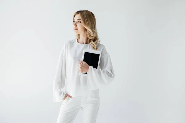 Молода приваблива жінка в білому одязі з планшетом позує ізольовано на сірому — стокове фото