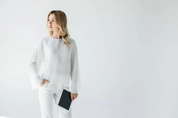 Portrait de jeune femme songeuse vêtue de blanc avec tablette isolée sur gris — Photo de stock