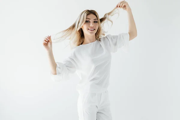 Portrait de femme blonde souriante en vêtements blancs jouant avec les cheveux isolés sur blanc — Photo de stock