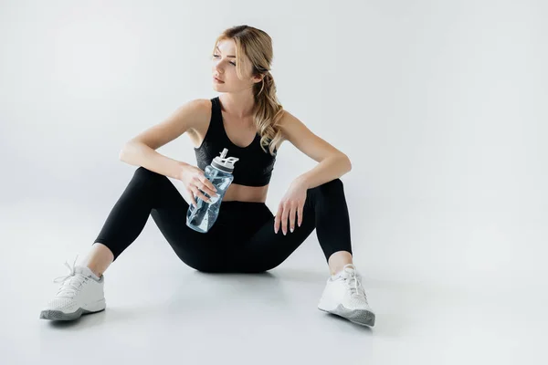 Mujer atlética en ropa deportiva negra con botella de agua deportiva aislada en gris - foto de stock