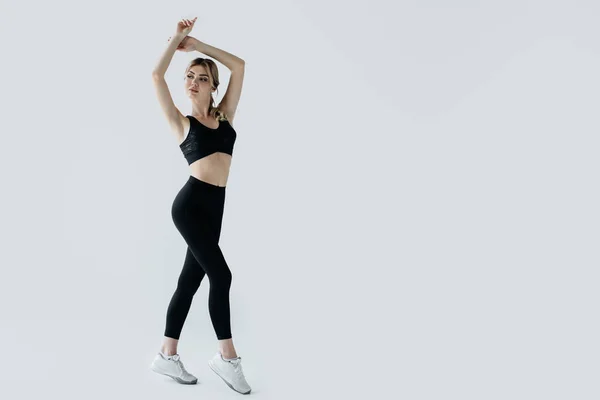 Молода блондинка спортсменка в чорному спортивному одязі позує ізольовано на сірому — стокове фото